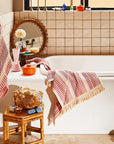 A pink and ivory striped waffle knit hand towel with tassel detailing on each end.