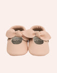 Baby moccasins made of soft leather in a light pink shade with a bow on the top.
