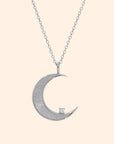 A gold necklace with a moon shaped pendant and a cz stone on the edge.