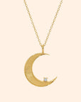 A gold necklace with a moon shaped pendant and a cz stone on the edge.