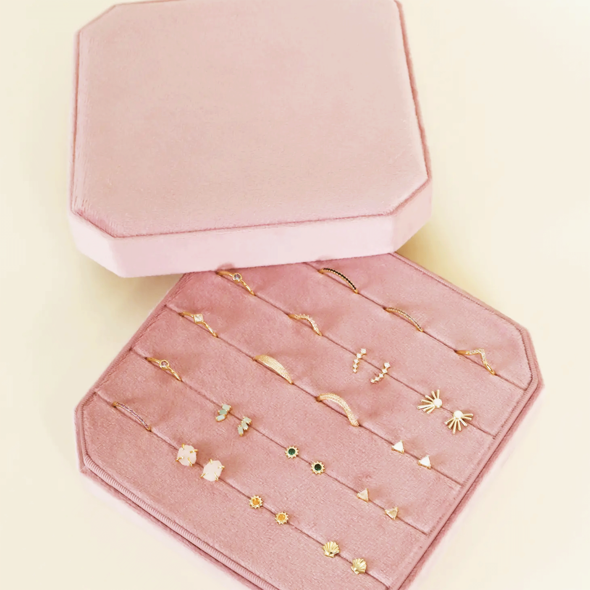On a white background is a light pink velvet jewelry box filled with earrings and rings that are not included with purchase. 