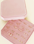 On a white background is a light pink velvet jewelry box filled with earrings and rings that are not included with purchase.