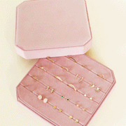 On a white background is a light pink velvet jewelry box filled with earrings and rings that are not included with purchase.