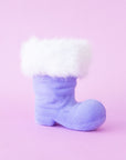 A lavender velvet Santa boot ornament with white fur sits on a pink background.