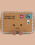 A brown letter shaped stuffed toy with a smiling face and brown legs and feet and text on the top left that reads, 'To Santa Claus The North Pole'.