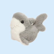 On a blue background is a grey and white shark stuffed animal toy.