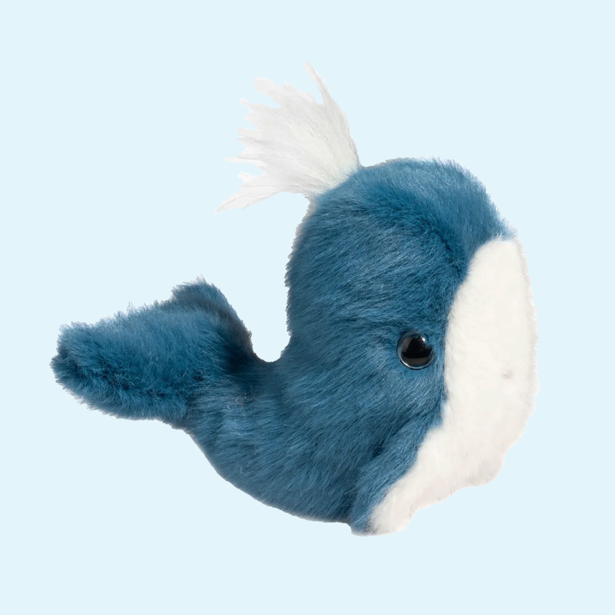 On a blue background is a fluffy blue and white whale stuffed animal toy. 