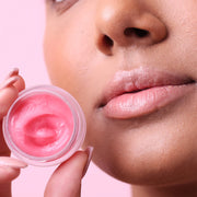 A model holding a small jar of pink lip balm.