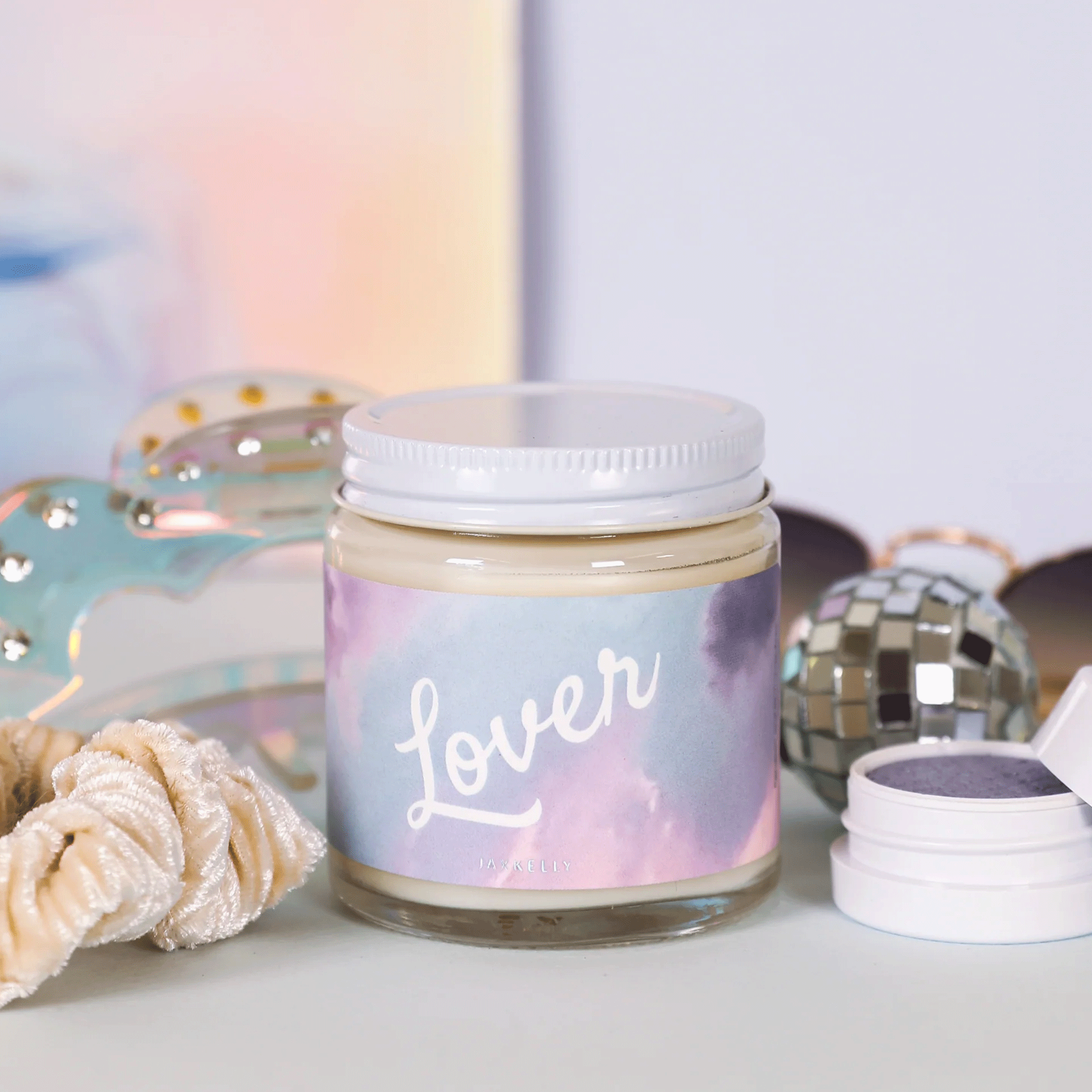 A pink and purple cloud label that reads, "Lover" on a glass jar candle with a white lid.