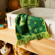 A green floral and leaf print face towel with a fringe edge.