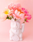 A ceramic lucky cat vase in white with its paw up in the waving position staged here with natural florals.