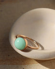 A thin gold ring with a green chrysoprase stone in the center.