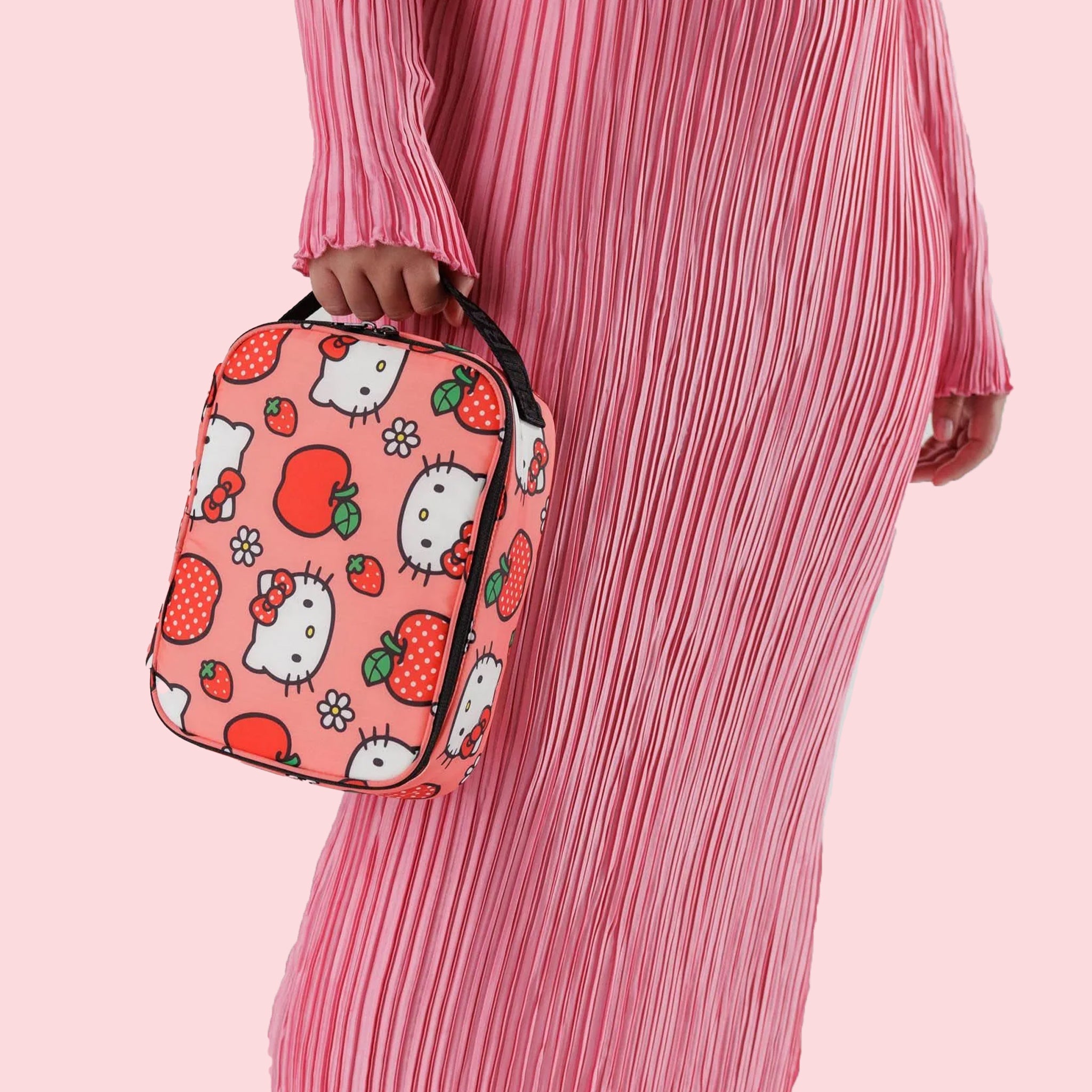 A pink and red lunch box with a Hello Kitty Apple pattern and black strap. 