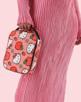 A pink and red lunch box with a Hello Kitty Apple pattern and black strap.