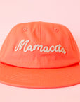 A coral orange flat brim hat with ivory embroidering that reads, 'Mamacita'.