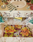Red rectangular bath mat with a colorful floral print and beige tassels is shown on a bathroom floor.