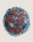 A blue round pillow with red and blue florals with a fringe edge.