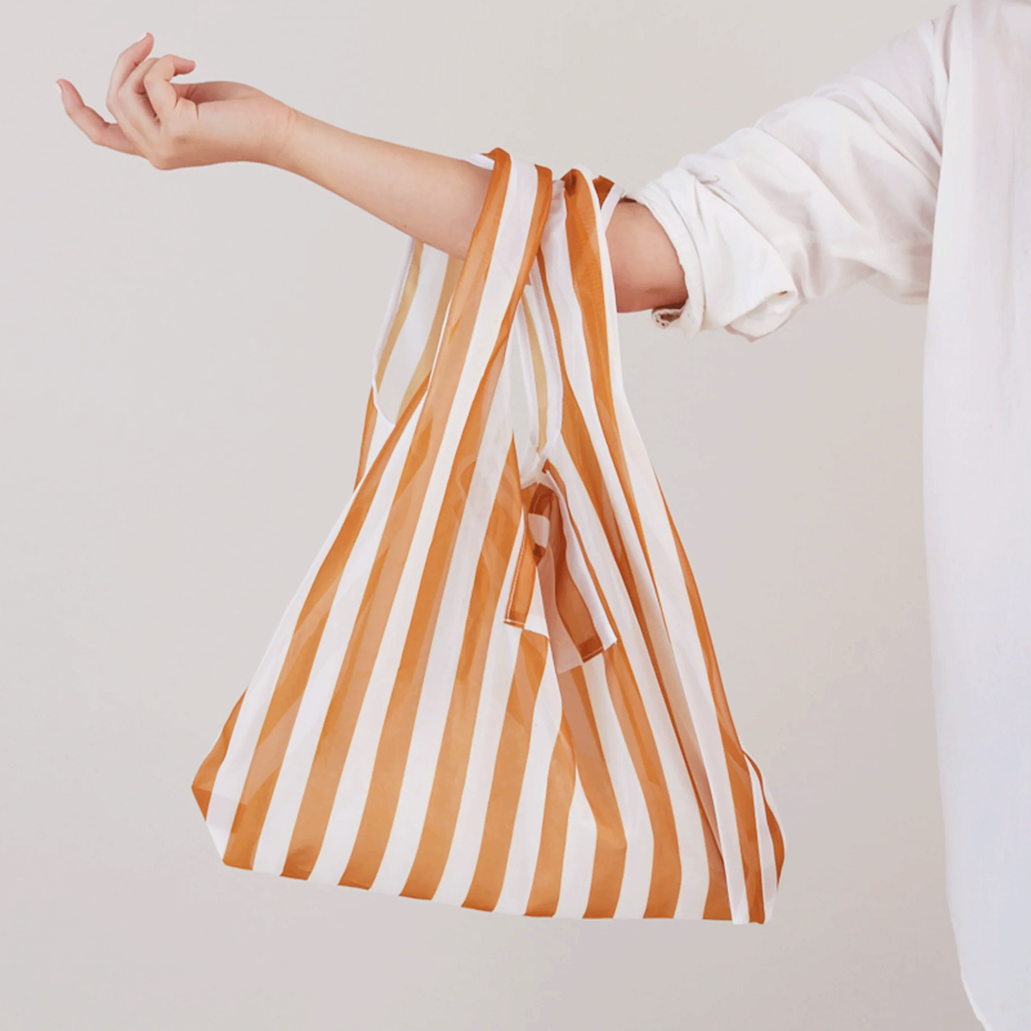 On a white background is a white and orange striped nylon tote. 