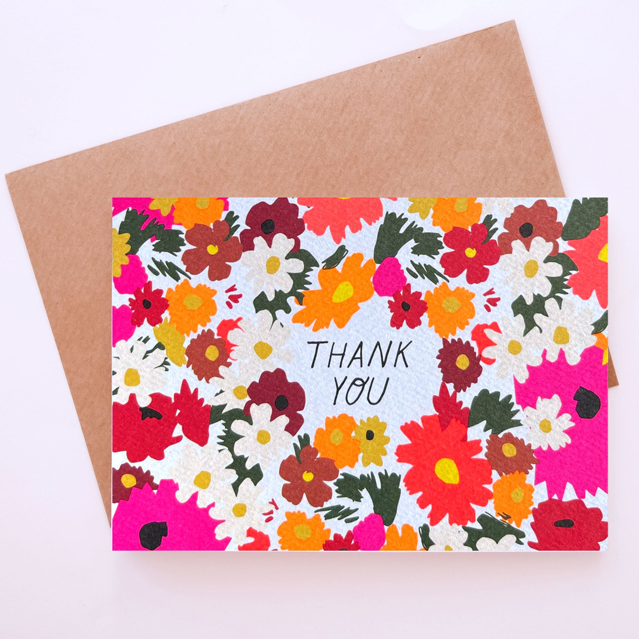 On a neutral background is a floral print card with red, white, orange and pink flowers on the front as well as text in the center that reads, "Thank You". 