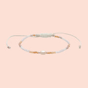 A peachy and white beaded bracelet with an adjustable cord detail. 