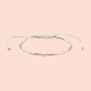 A peachy and white beaded bracelet with an adjustable cord detail.