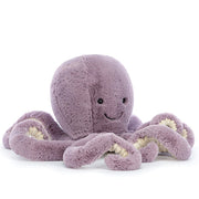 On a white background is a purple octopus stuffed animal with a smiling face. 