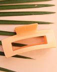 On a peachy background is a light orange claw clip with a rectangle shape.