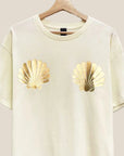 A short sleeved cream colored shirt with gold foiled shells on the chest area.