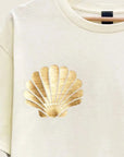 A short sleeved cream colored shirt with gold foiled shells on the chest area.