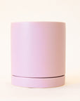 A lilac cylinder ceramic planter with a removable tray for watering in front of a tan background.
