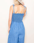 A mid blue shade of denim in a smocked jumpsuit with tie shoulder straps.