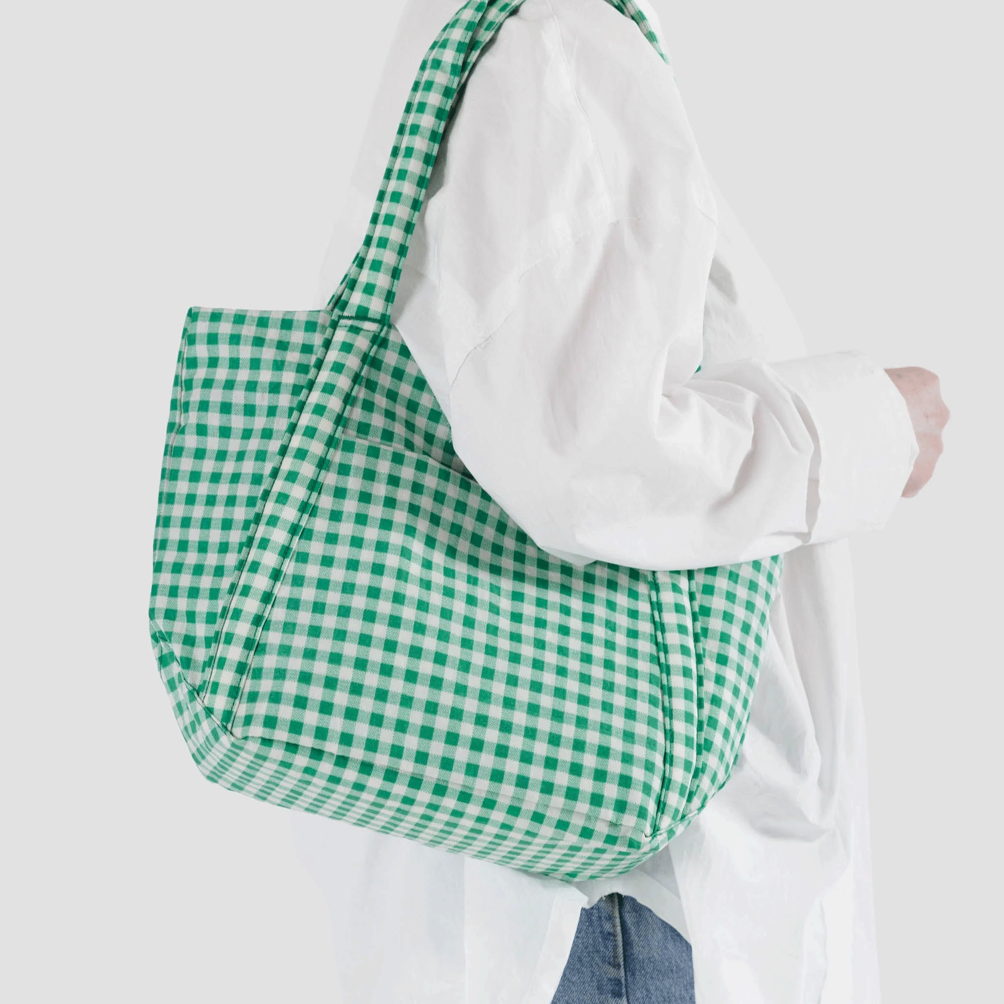 On a white background is a green and white gingham printed tote bag worn on a model.