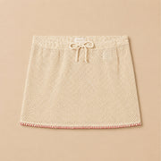 A tan crochet knit skirt with a red woven edge detail.