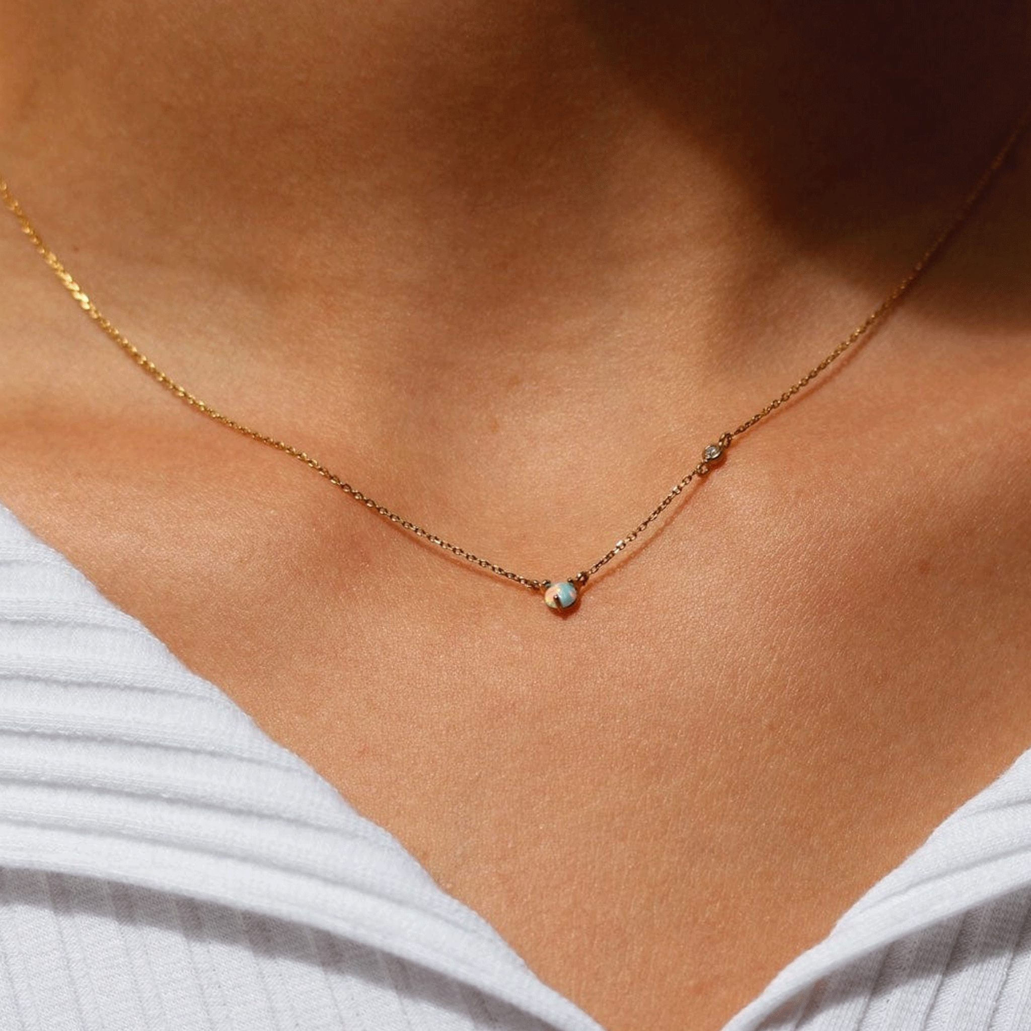 A dainty gold chain necklace with a circular opal stone in the center worn on a model.
