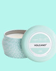 A small blue tin candle with white wax and a white diamond repeating pattern on the outside of the tin. Comes with a matching blue lid that reads, "Capri Blue Volcano".