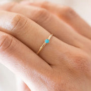 A gold thin band ring with a single mini turquoise stone in the center.
