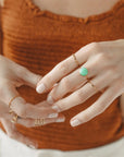 A minimal gold band ring worn on a model with their other rings.