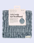 A fuzzy light blue extra wide headband folded up in its packaging that has a white label and black text that reads, "Extra Wide Spa Headband".