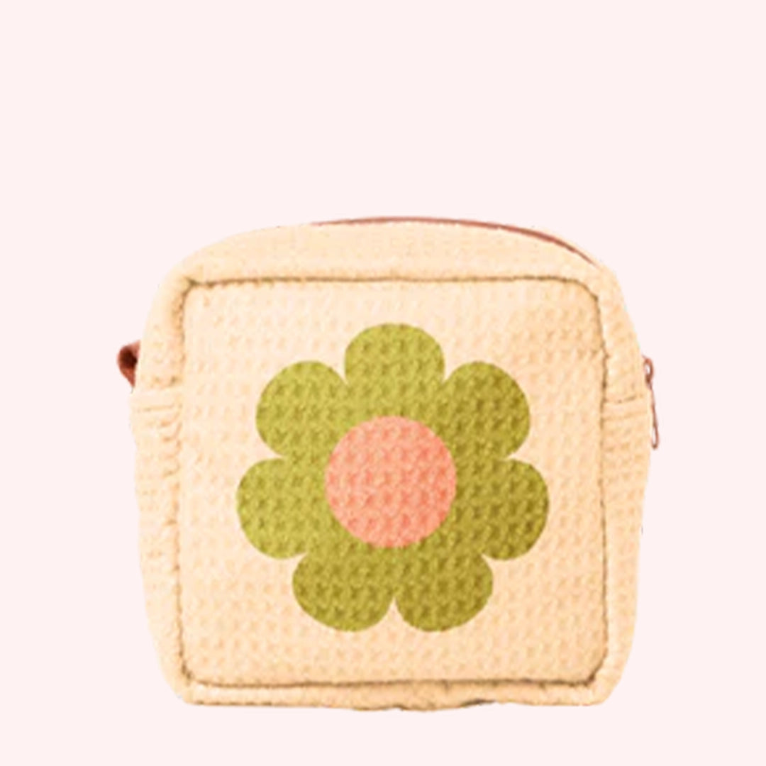 On a white background is a light yellow waffle textured pouch with a green and orange daisy in the center. 