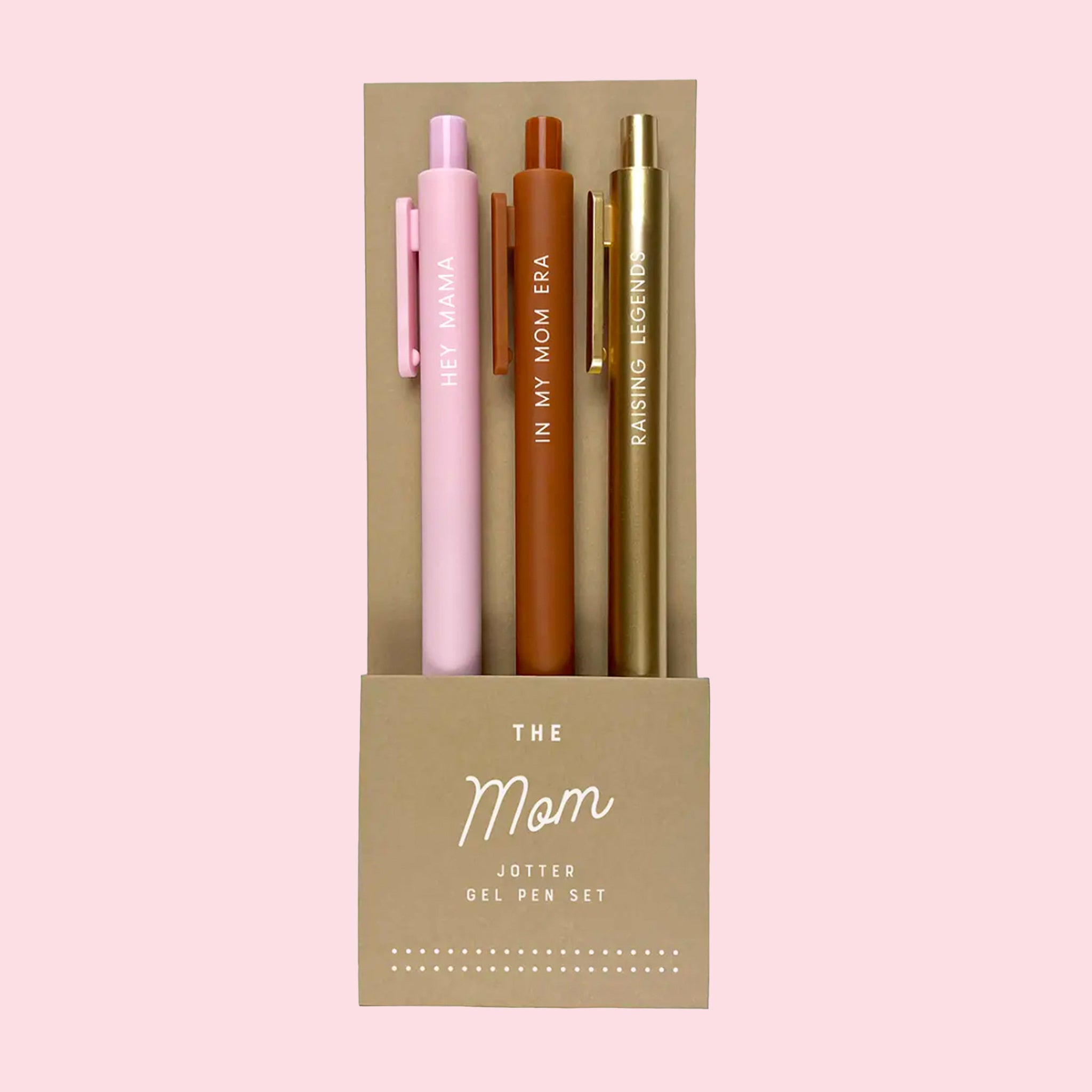 On a pink background is a set of three different colored pens, one pink, one terracotta, and the other gold with phrases on each pen. 