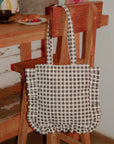A black and white gingham print tote bag with ruffle details and shoulder straps.