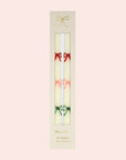A set of two white taper candles with red, pink and green bow designs.