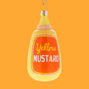 A glass ornament of a bottle of yellow mustard, the ornament is yellow with an orange label that reads, "yellow mustard".