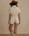 A natural colored short sleeve jumpsuit with a cinched waist and front pockets as well as a stitched rope heart detail on the back.