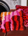 A multi colored shag pillow in orange, brown, pink and yellow shades.