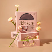 A three piece set that includes on light pink satin pillow case, one brown sleep mask and one light pink scrunchie.