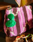 A pink terry cloth pouch with a green tassel on the zipper closure.