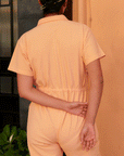 A model wearing a light peach colored short sleeve jumpsuit with a zipper up the front and a collar.