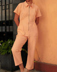 A model wearing a light peach colored short sleeve jumpsuit with a zipper up the front and a collar.
