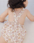 A children's romper with a light pink and yellow floral pattern.